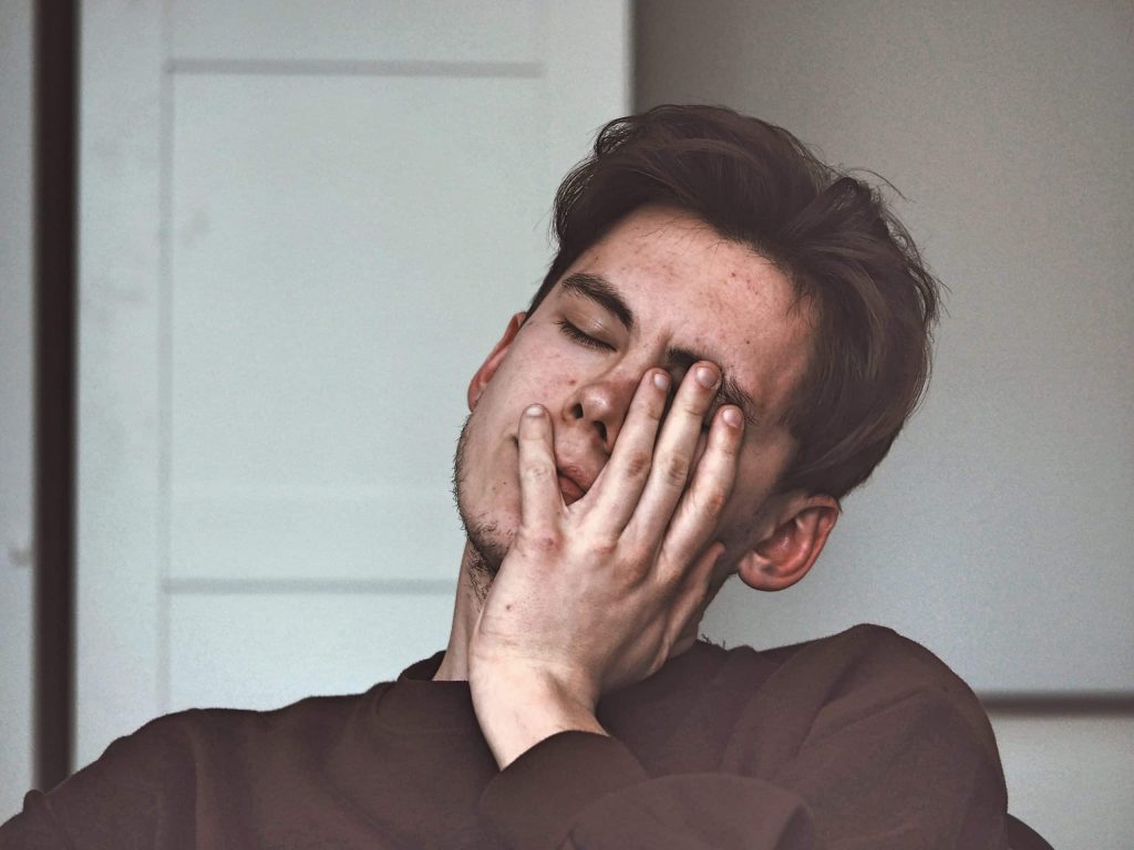 Burn-out en burn-outklachten. Jonge man zit vermoeid met hand voor gezicht.
