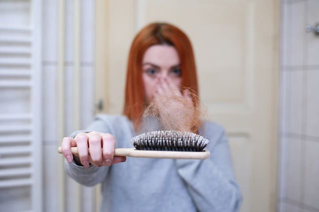 Haaruitval en stress. Vrouw met borstel met haar in haar hand